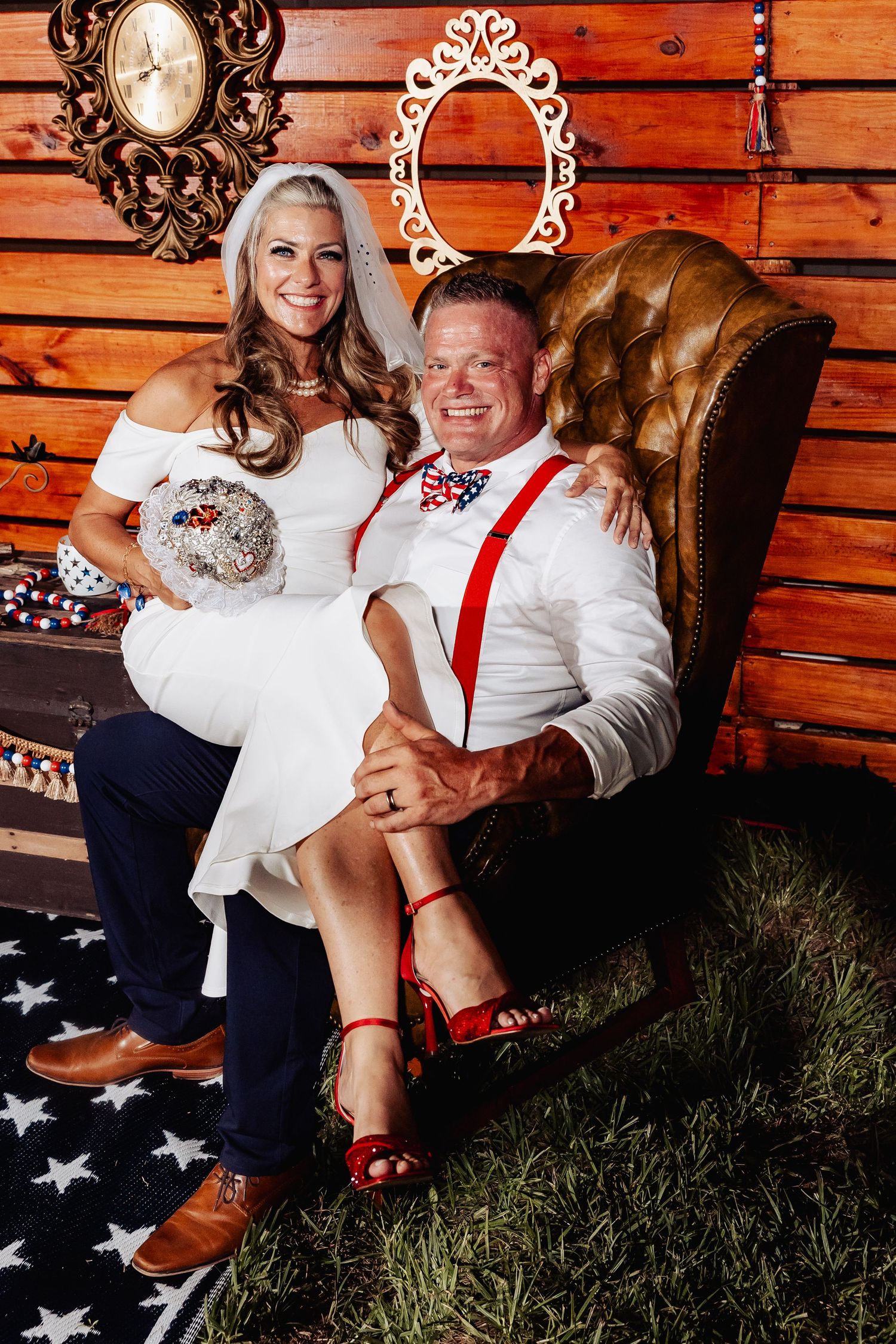 Bride and groom posing together in leather chair at patriotic-themed rustic barn wedding reception.