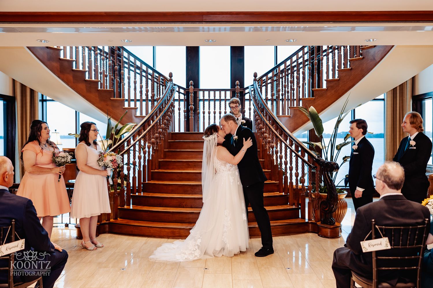 Wedding ceremony taking place on grand wooden staircase with guests watching from below.