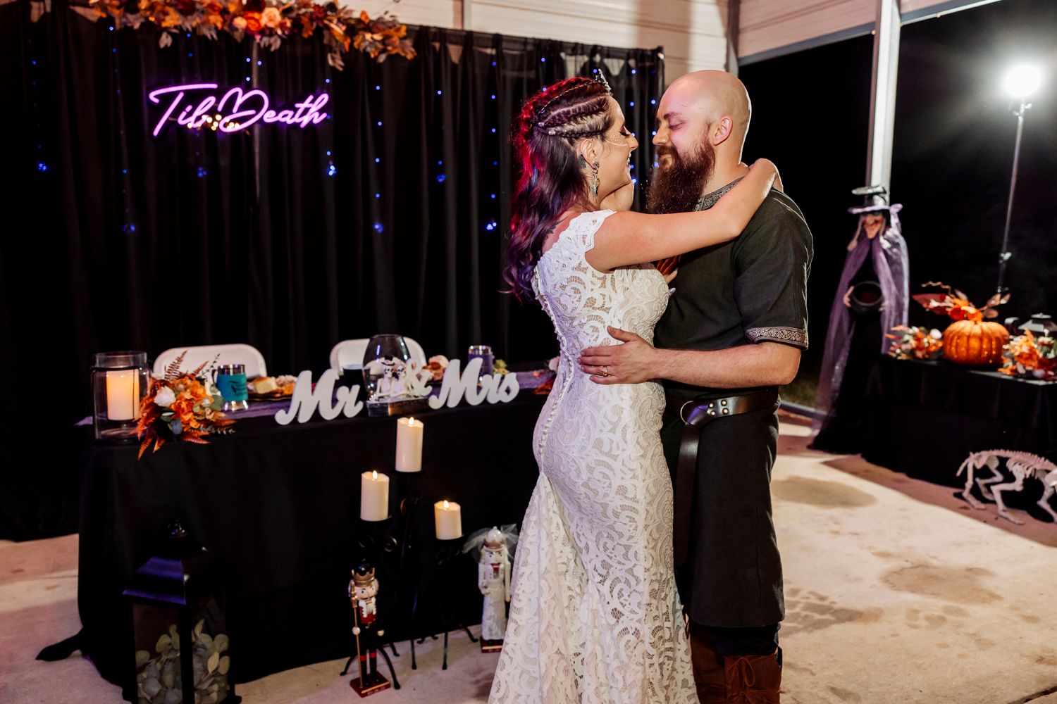 A couple shares an intimate dance moment under neon lighting at their medieval-themed wedding reception.