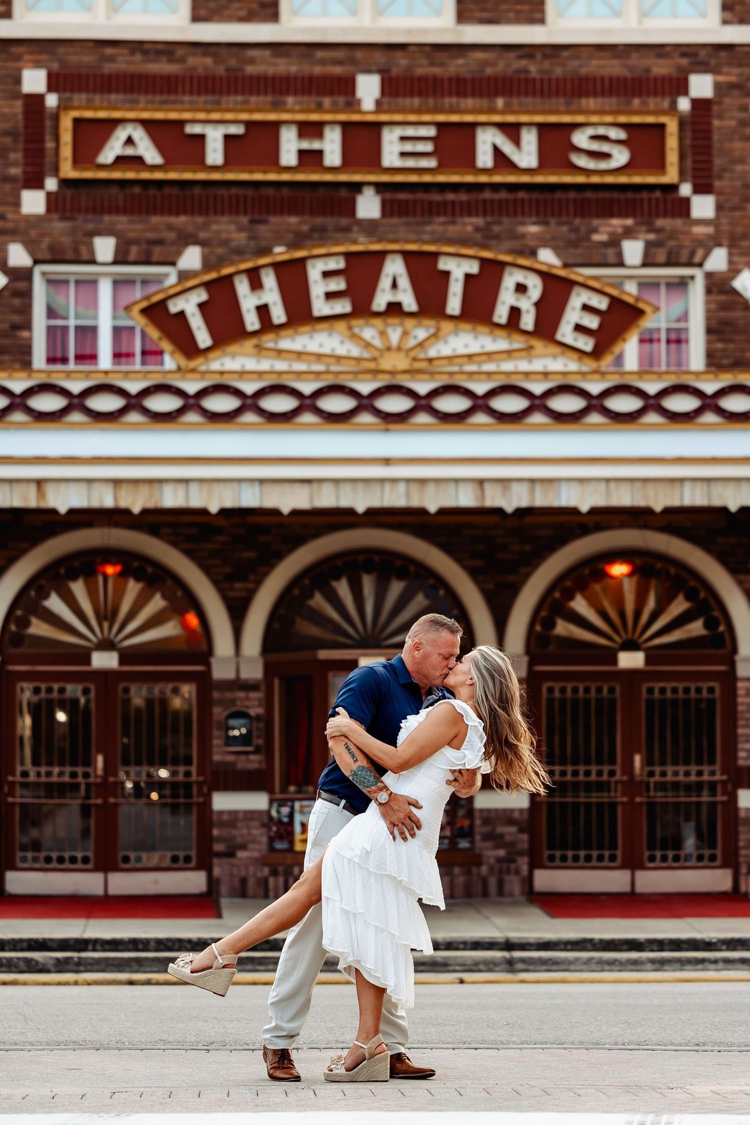 Couple sharing a romantic dip kiss in front of the historic Athens Theatre marquee sign.