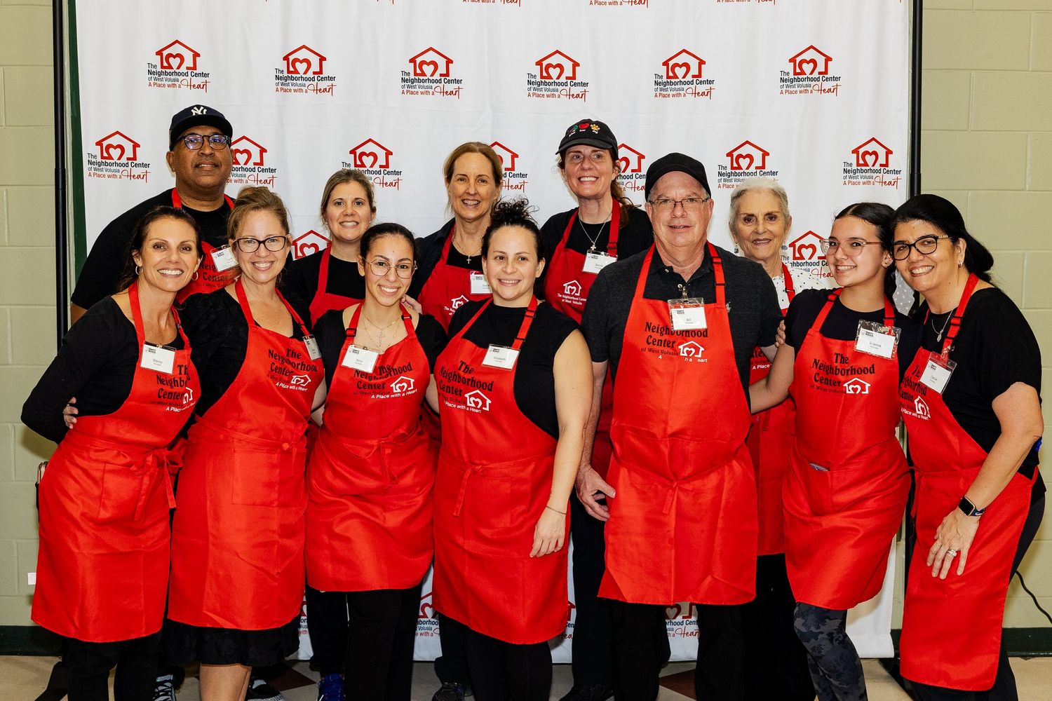 Group of volunteers in red aprons posing together at a charity event in front of a branded backdrop.