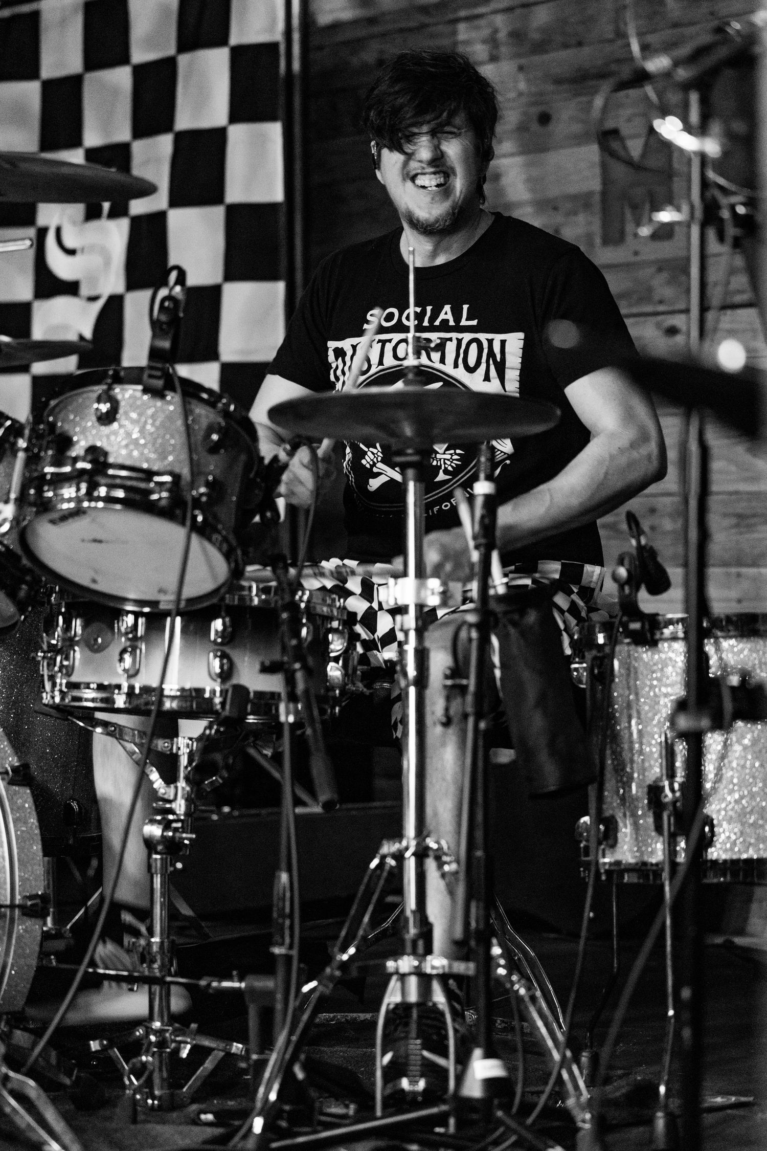 Smiling drummer performing on stage in black and white photo wearing a Social Distortion shirt.