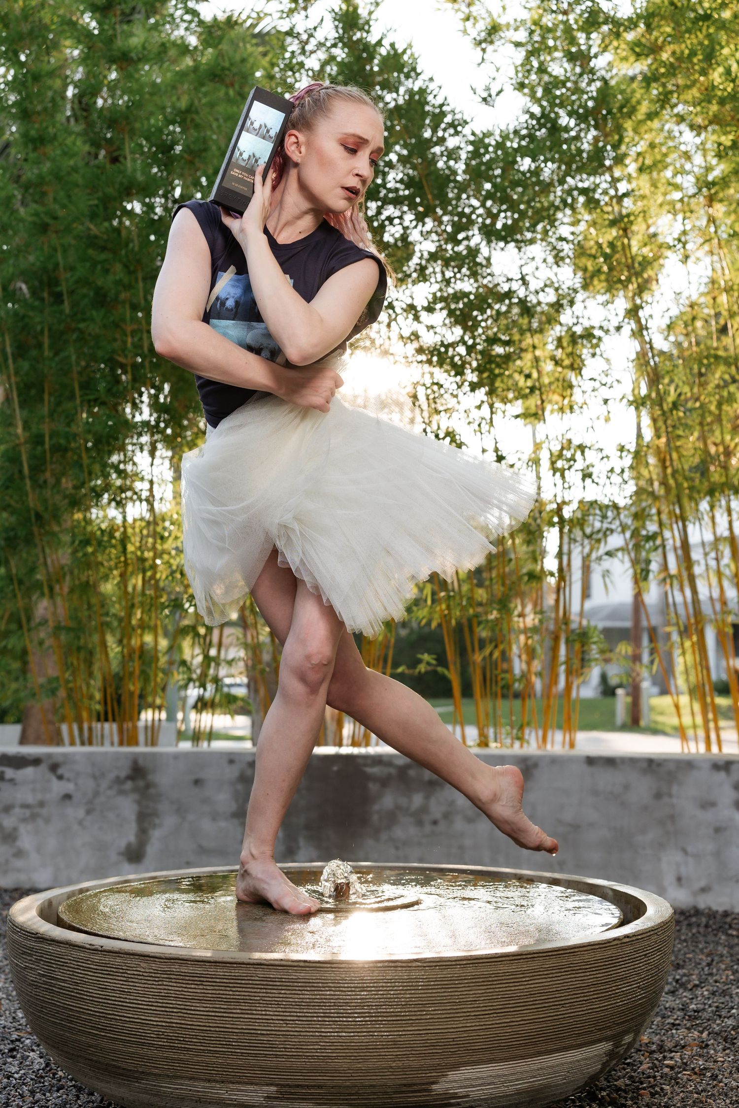 Ballerina in white tutu and black top poses gracefully in a decorative water bowl surrounded by bamboo trees.