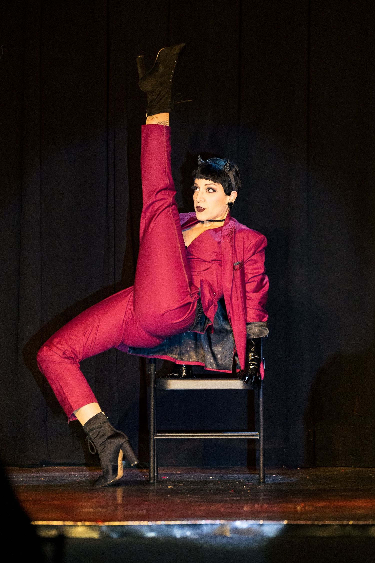 A performer in a red suit balances on a chair with one leg raised high on stage.