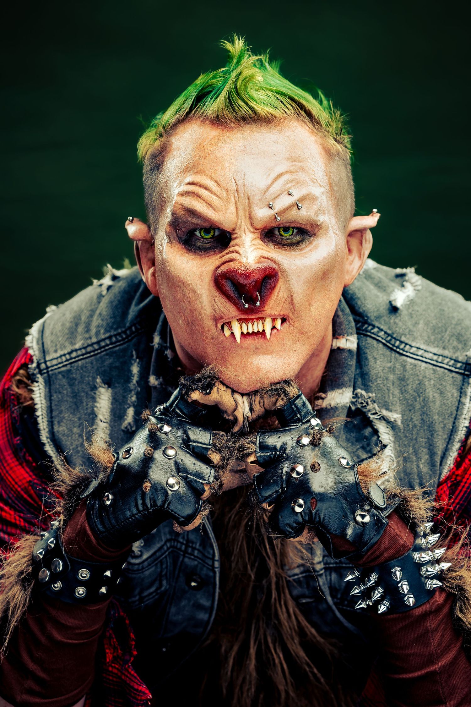Menacing punk troll costume featuring green mohawk hair, pointed ears, fangs, and studded leather gloves on dark backdrop.