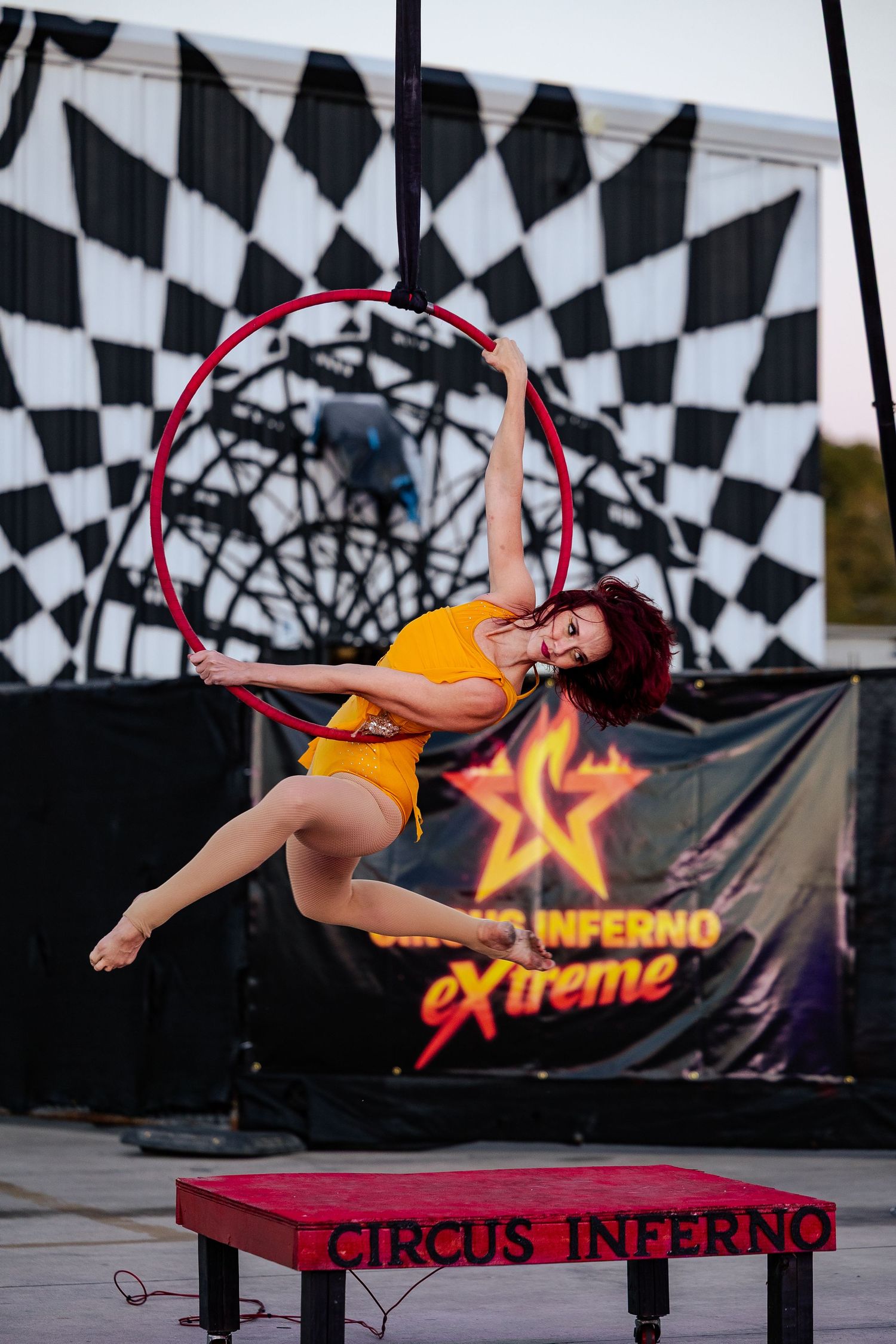 Female aerialist in yellow outfit performing on a red aerial hoop at Circus Inferno Extreme show.
