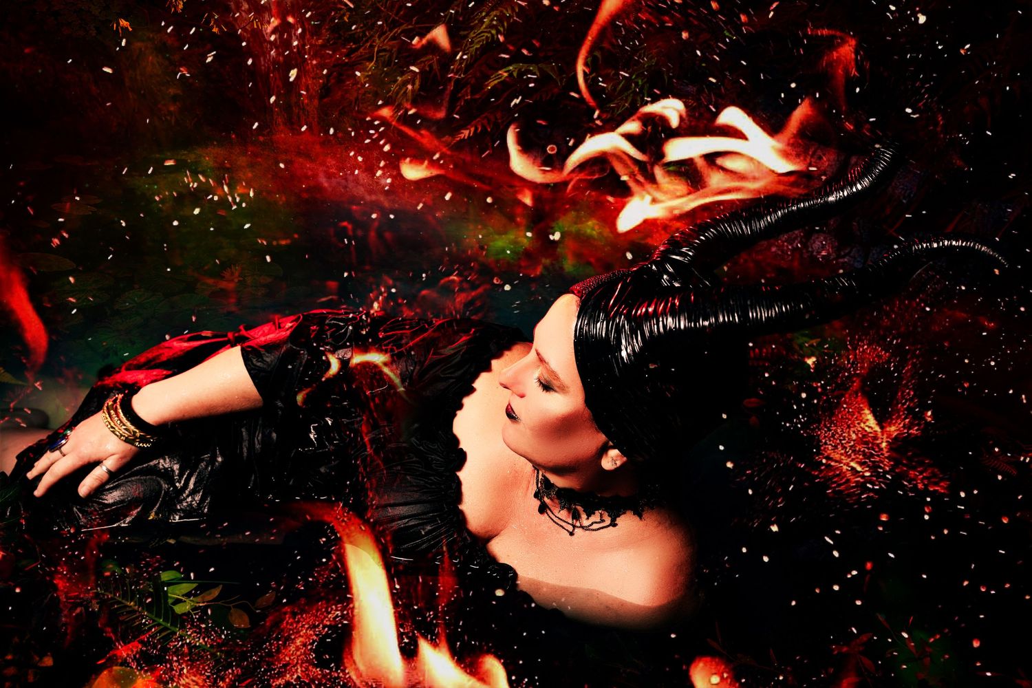 Woman in black Maleficent horns and costume surrounded by fire sparks in dramatic dark fantasy scene.