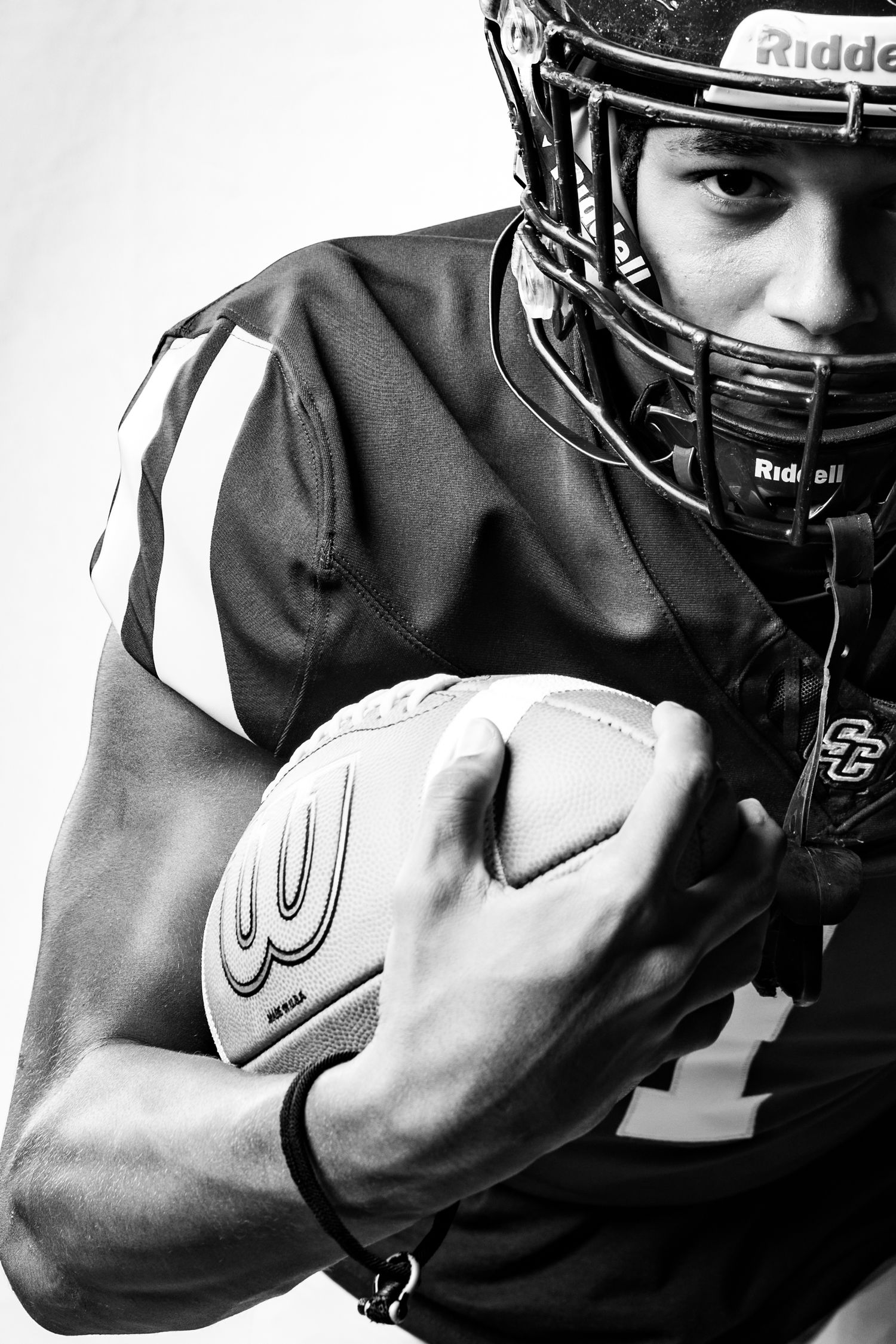 Dramatic black and white portrait of football player wearing helmet and holding ball.