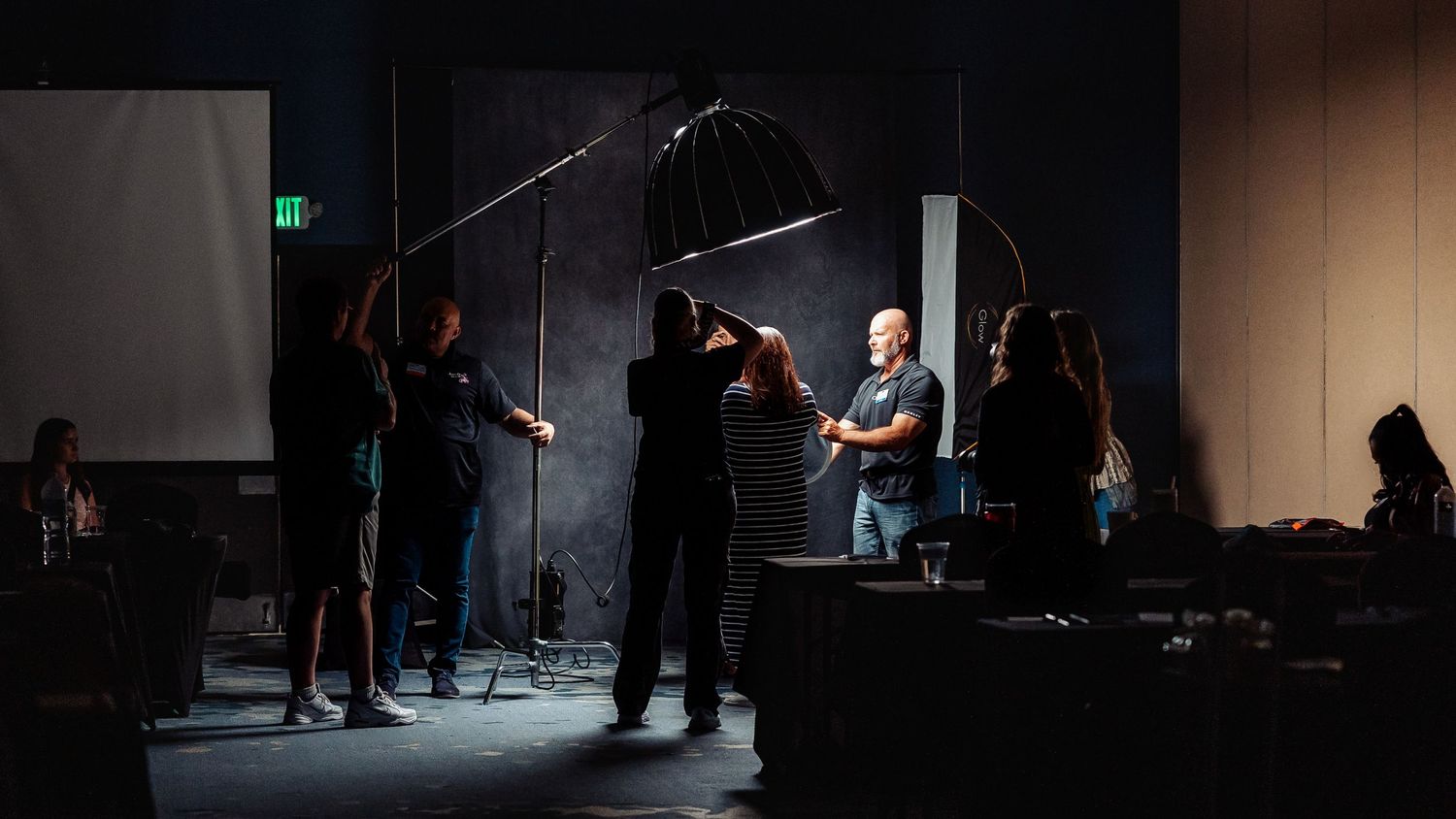 Behind the scenes photo shoot setup with crew and lighting equipment in a dark studio.