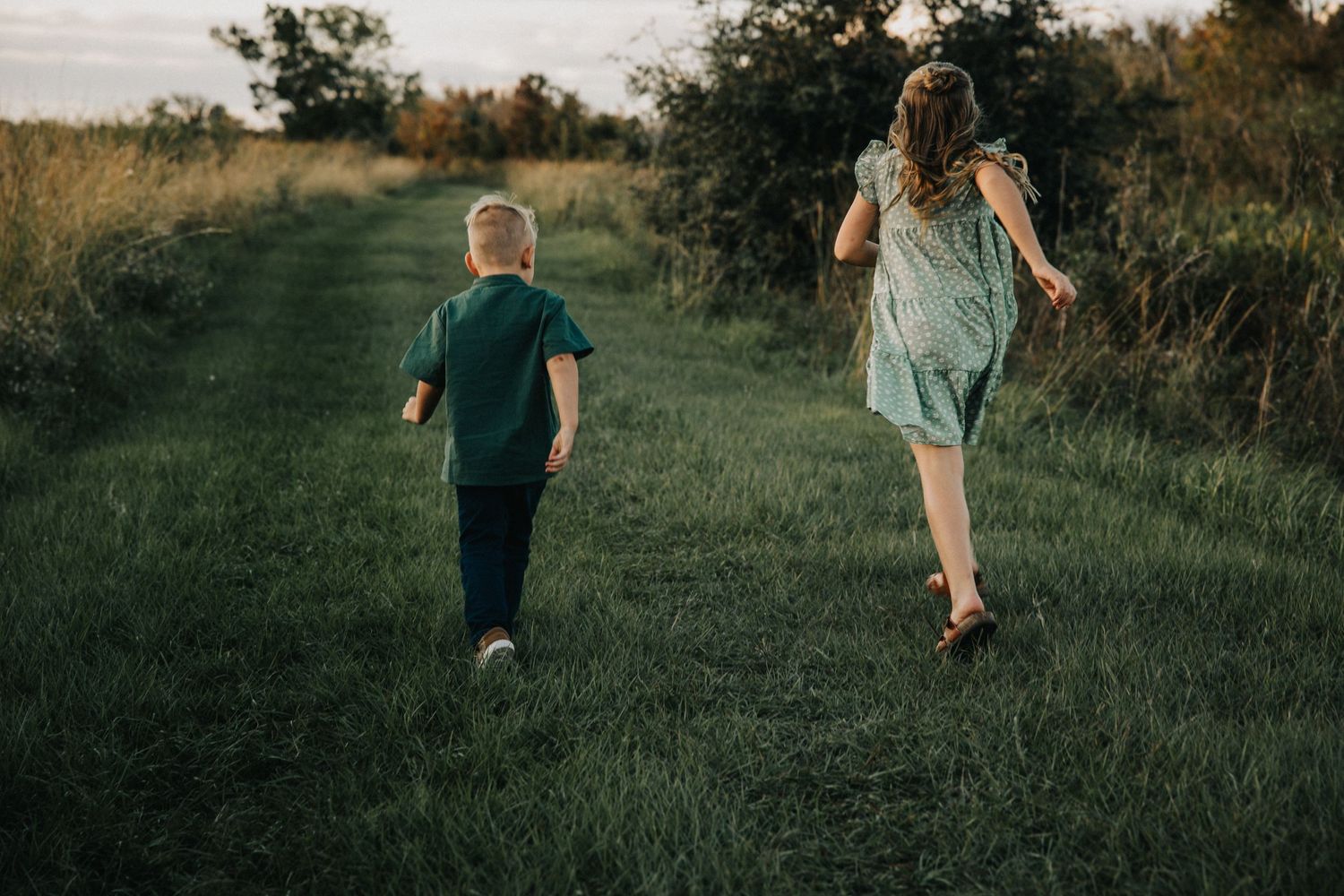 Two people running together on a grassy path at sunset with trees in background.