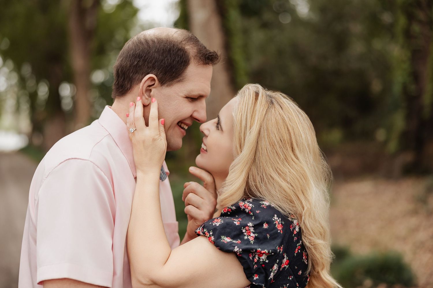 Couple sharing an intimate close moment smiling at each other outdoors among pine trees.