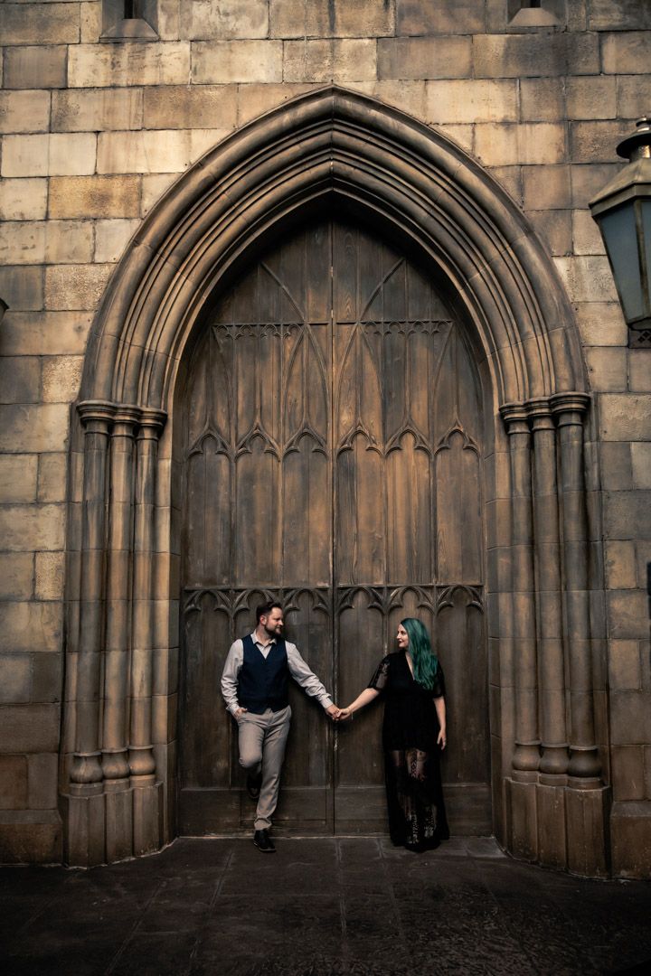 Couple holding hands in front of a grand Gothic arched wooden door at a stone cathedral.
