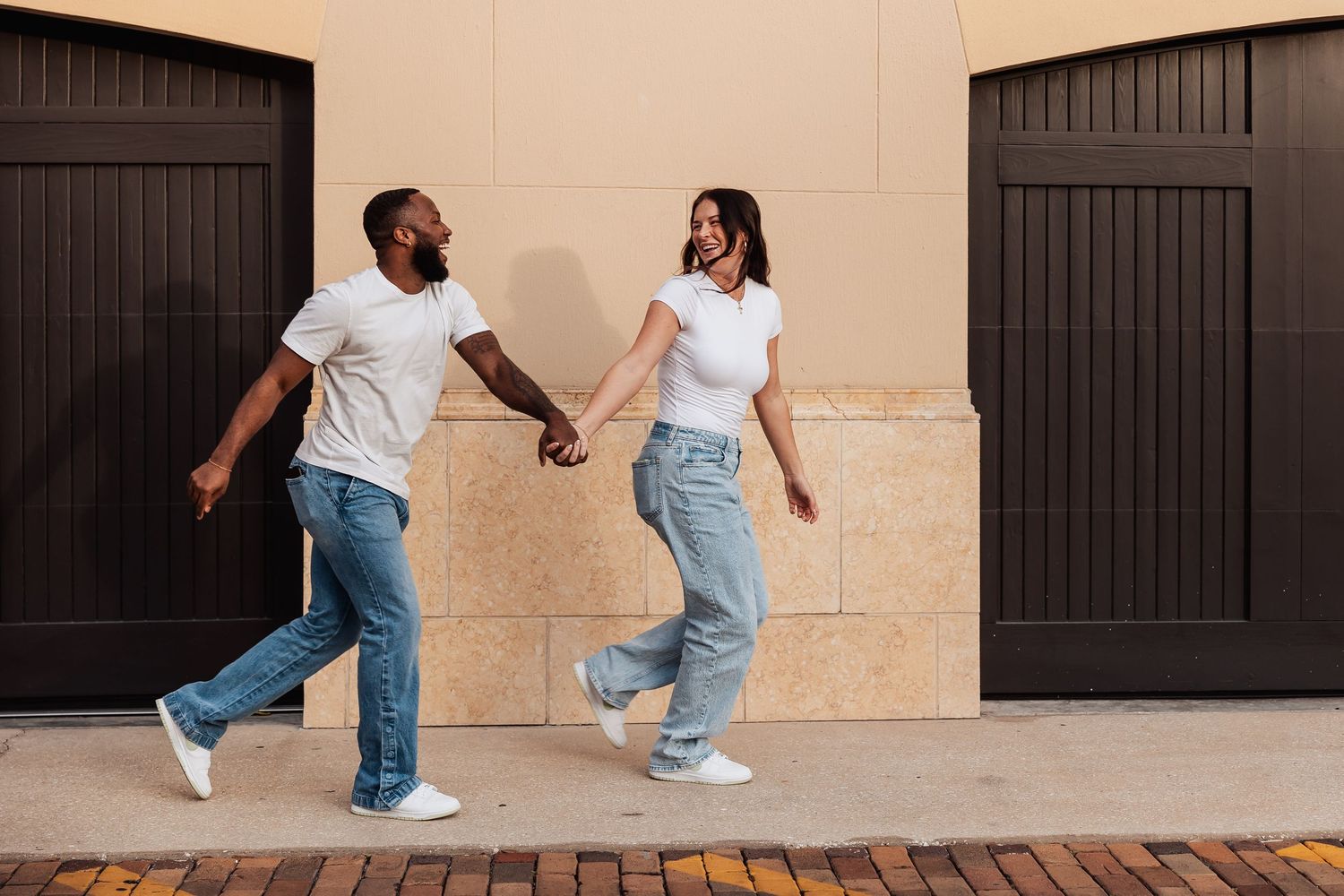 Happy interracial couple holding hands and walking together along a brick sidewalk.
