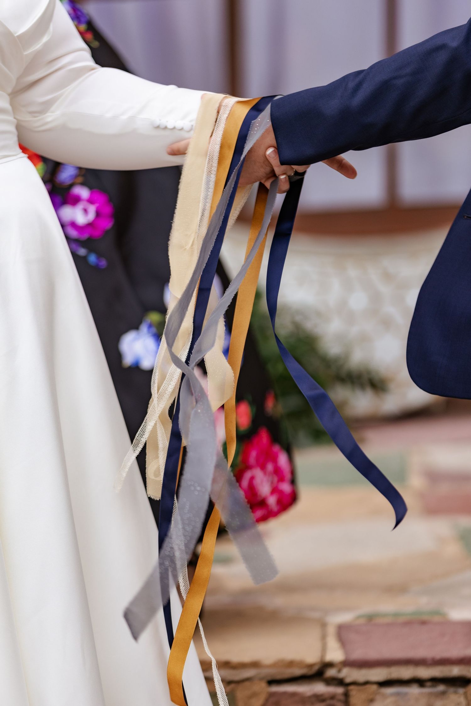 Close-up of handfasting ceremony with colorful ribbons binding bride and groom's hands together.