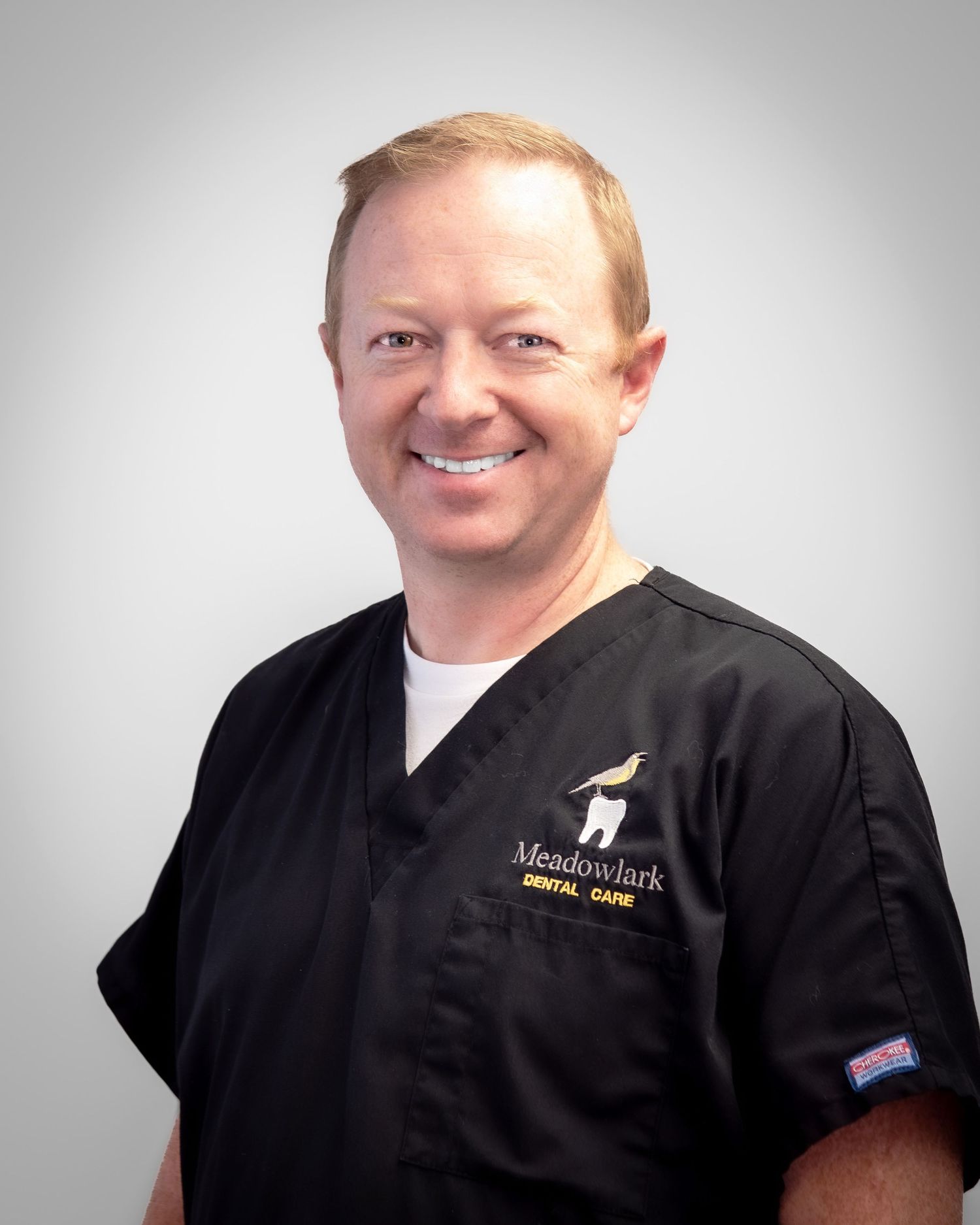 Smiling male dentist in black Meadowlark Dental Care scrubs poses for a professional headshot photo.