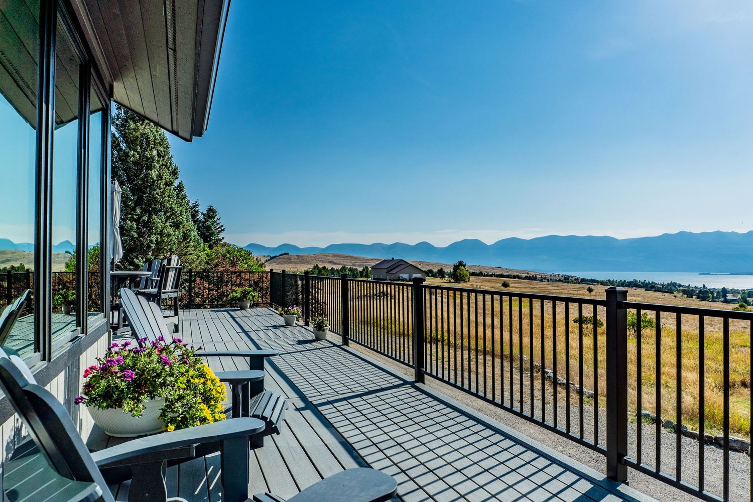 Expansive deck with Adirondack chairs offering stunning panoramic views of a lake and mountains under a clear blue sky.