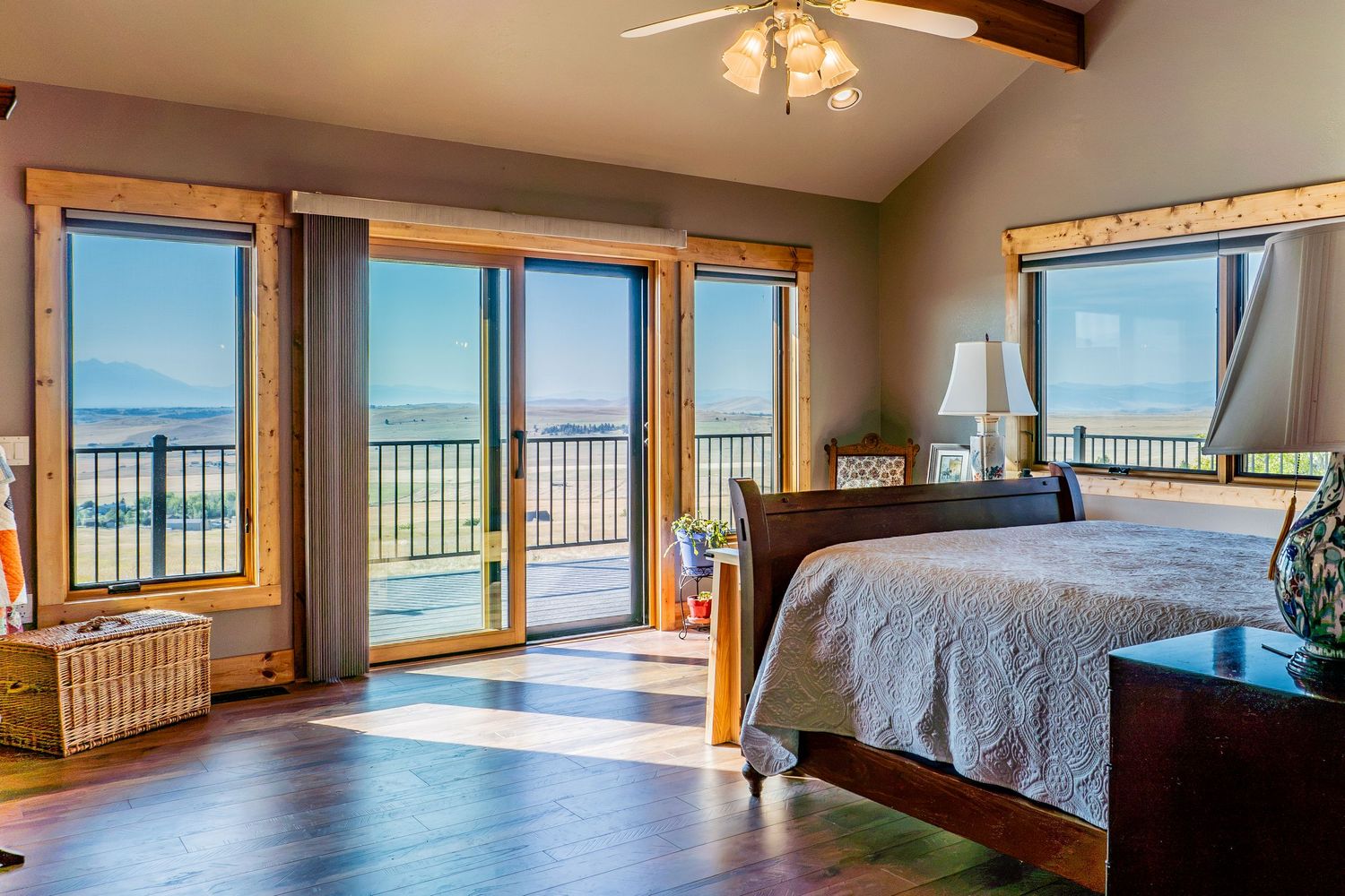 Bright bedroom with hardwood floors, wood-framed glass doors opening to a balcony with panoramic mountain and water views.