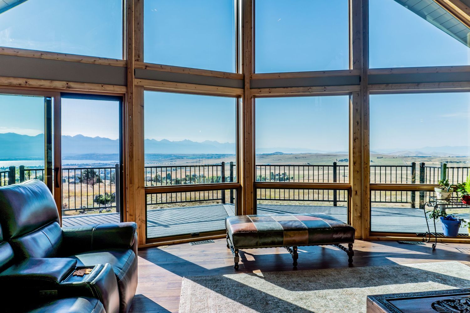 Luxury living room with floor-to-ceiling windows offering panoramic mountain and water views, featuring leather seating.