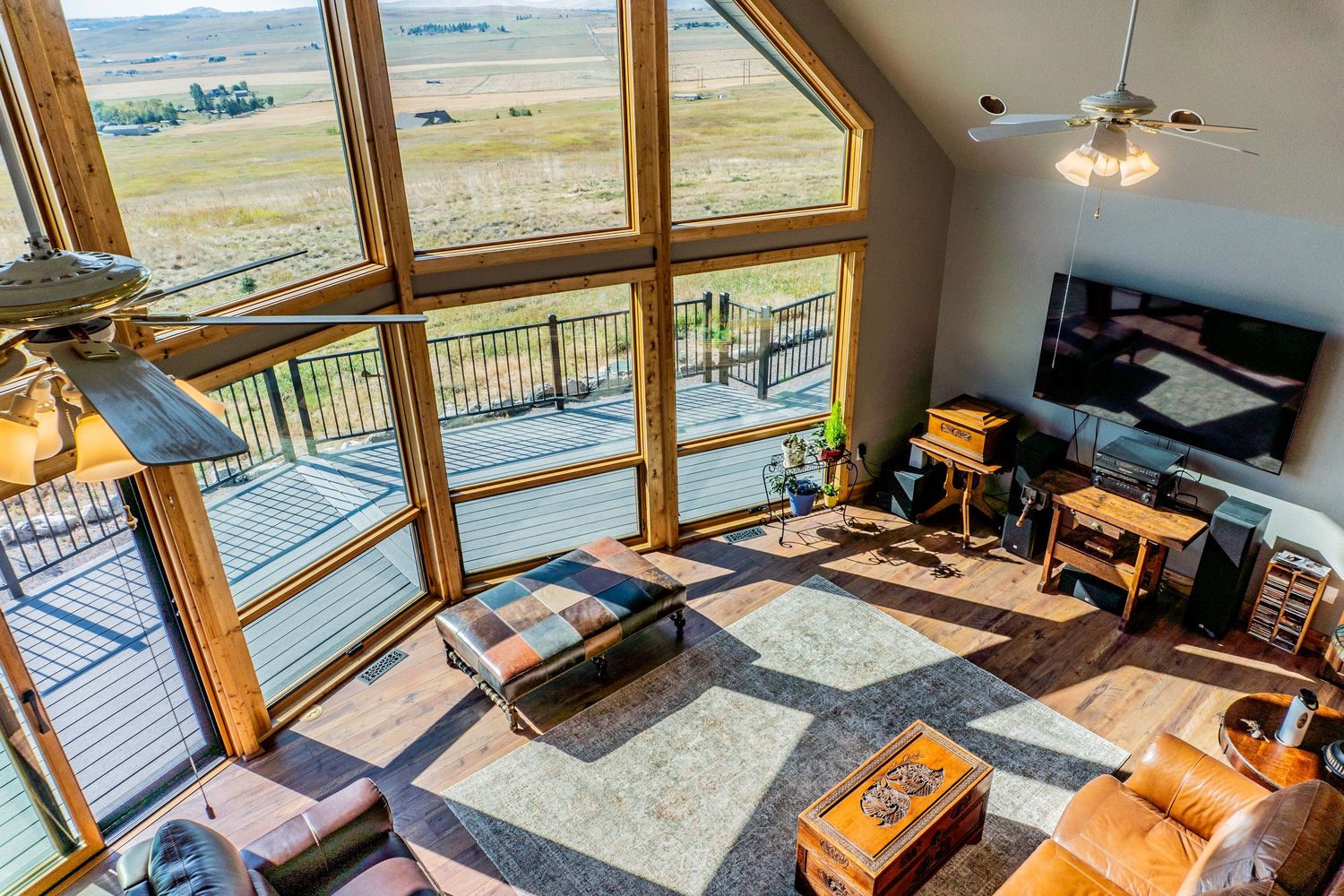 Aerial view of sunlit living room with floor-to-ceiling windows overlooking vast open plains and a wood deck.