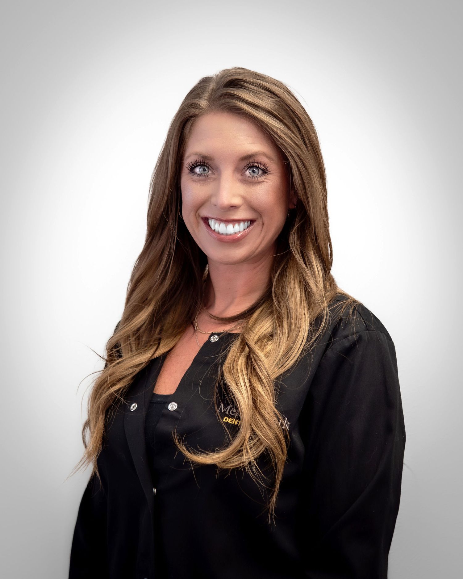 Professional headshot of a smiling woman with long blonde hair wearing a black uniform top.