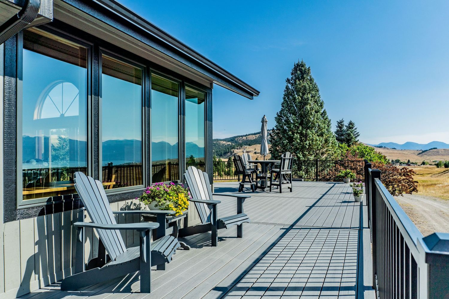 Spacious deck with Adirondack chairs overlooking stunning mountain views and lush green trees under a clear blue sky.