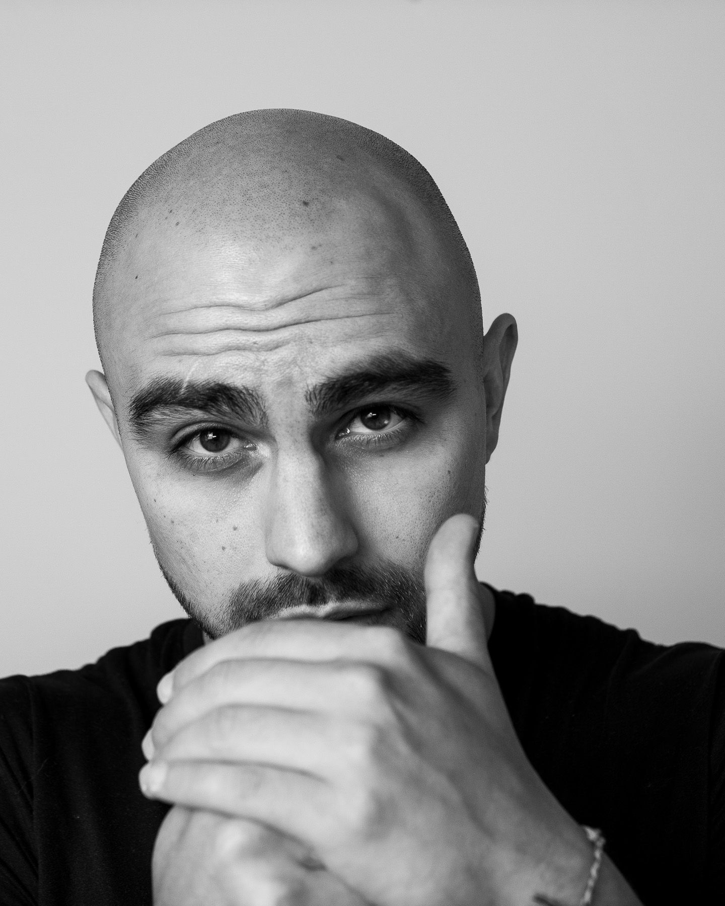 Black and white portrait of a bald man with goatee resting chin on hand, looking thoughtfully at camera.