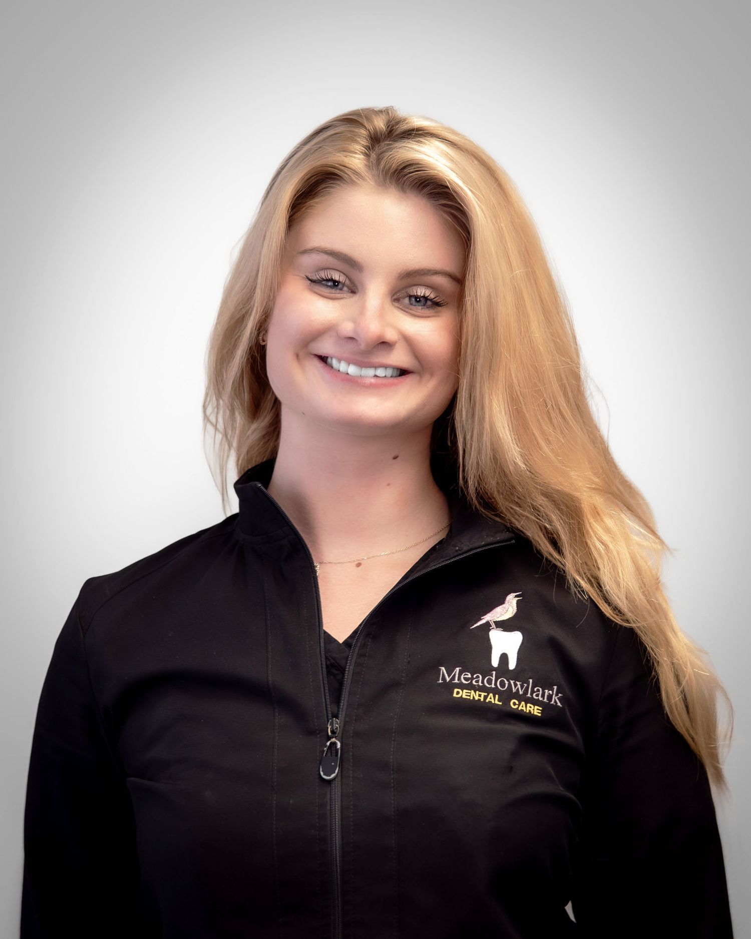 Smiling Meadowlark Dental Care staff member with blonde hair wearing a black branded jacket.