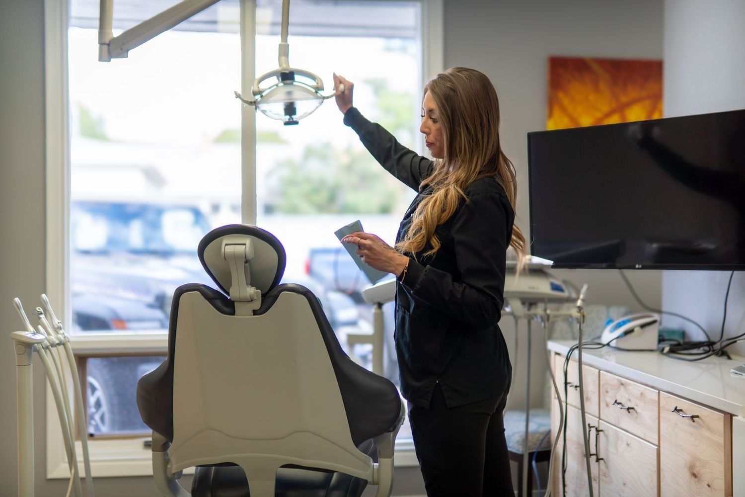 Dental professional adjusting exam light in modern dentist office with patient chair and equipment.