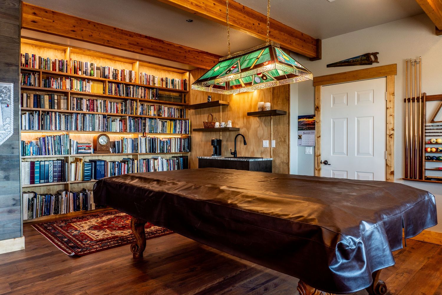 Cozy game room featuring a pool table, floor-to-ceiling bookshelves, and rustic wood accents with warm pendant lighting.