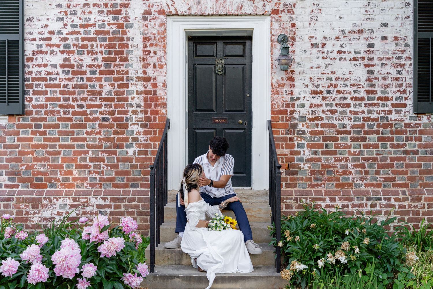 Couple sitting on brick building steps reading together surrounded by blooming pink hydrangeas. Taken by Row And Co Photography in FXBG VA