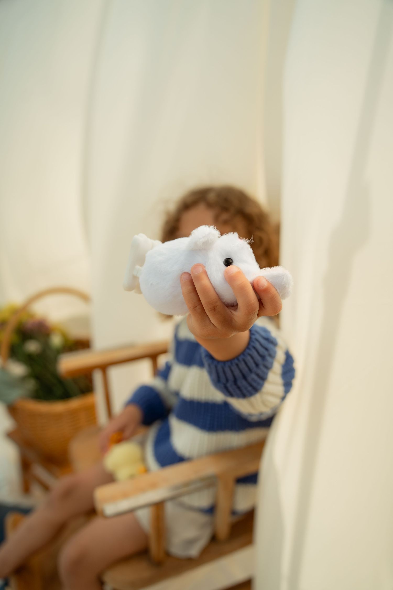 A curly-haired child holds up a white stuffed animal toy toward the camera inside a cozy tent. Taken by Row And Co Photography in FXBG VA