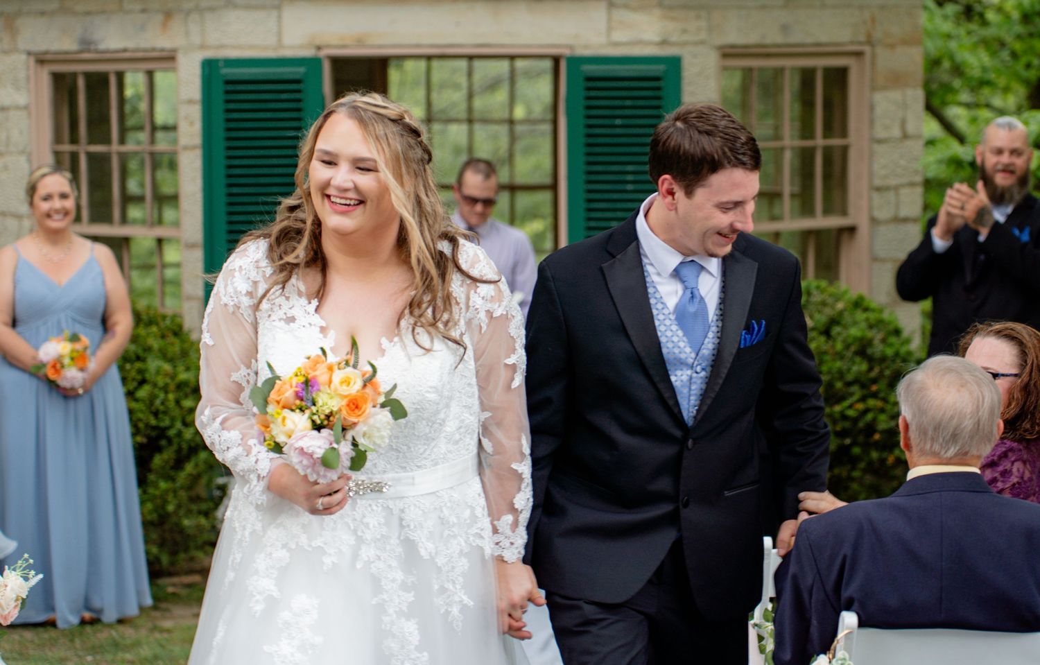 Smiling bride and groom walk down the aisle after wedding ceremony outdoors, bride holding colorful bouquet. Row and Co Photography