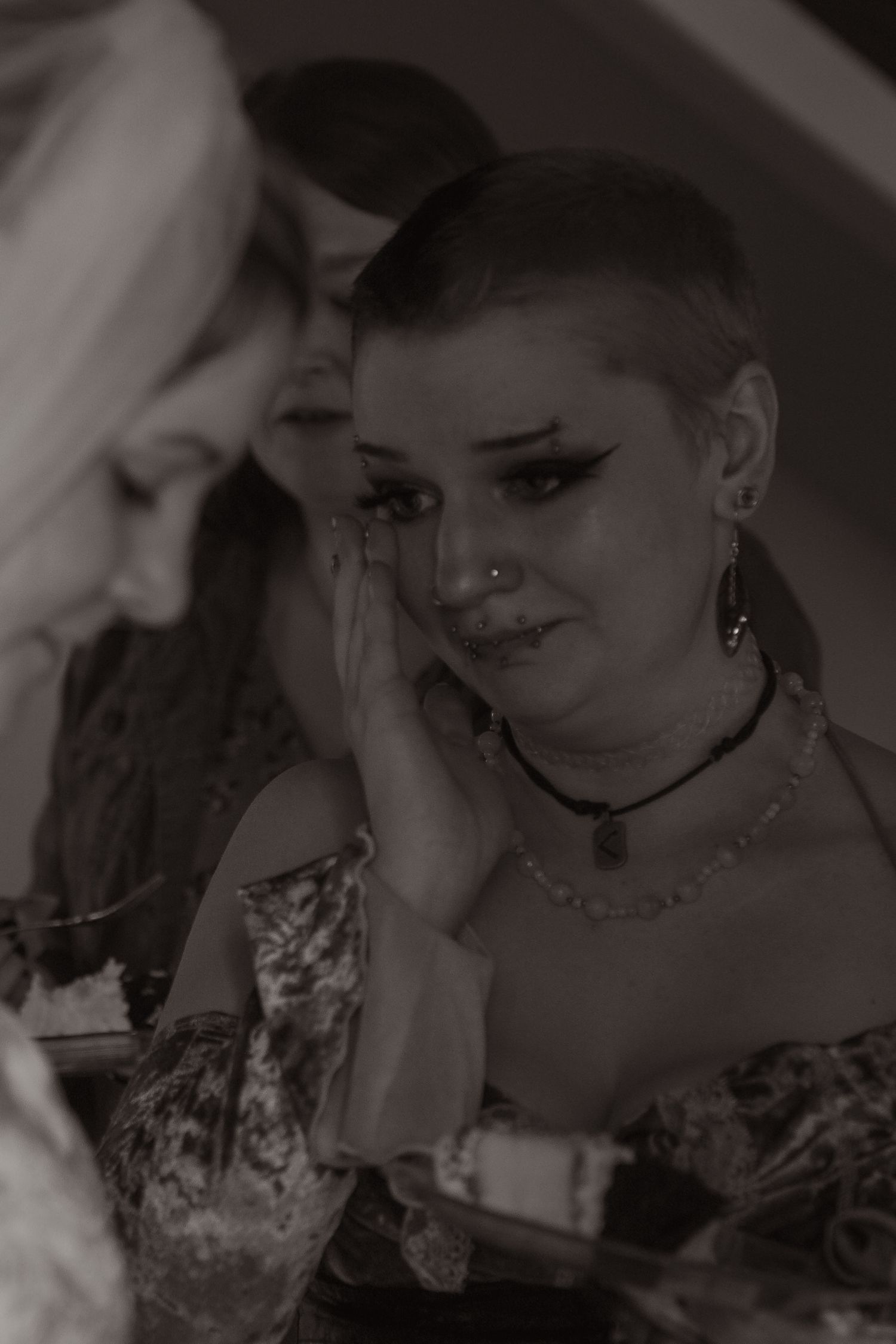 Emotional wedding guest wipes tears during ceremony in black and white photo capturing heartfelt moment.