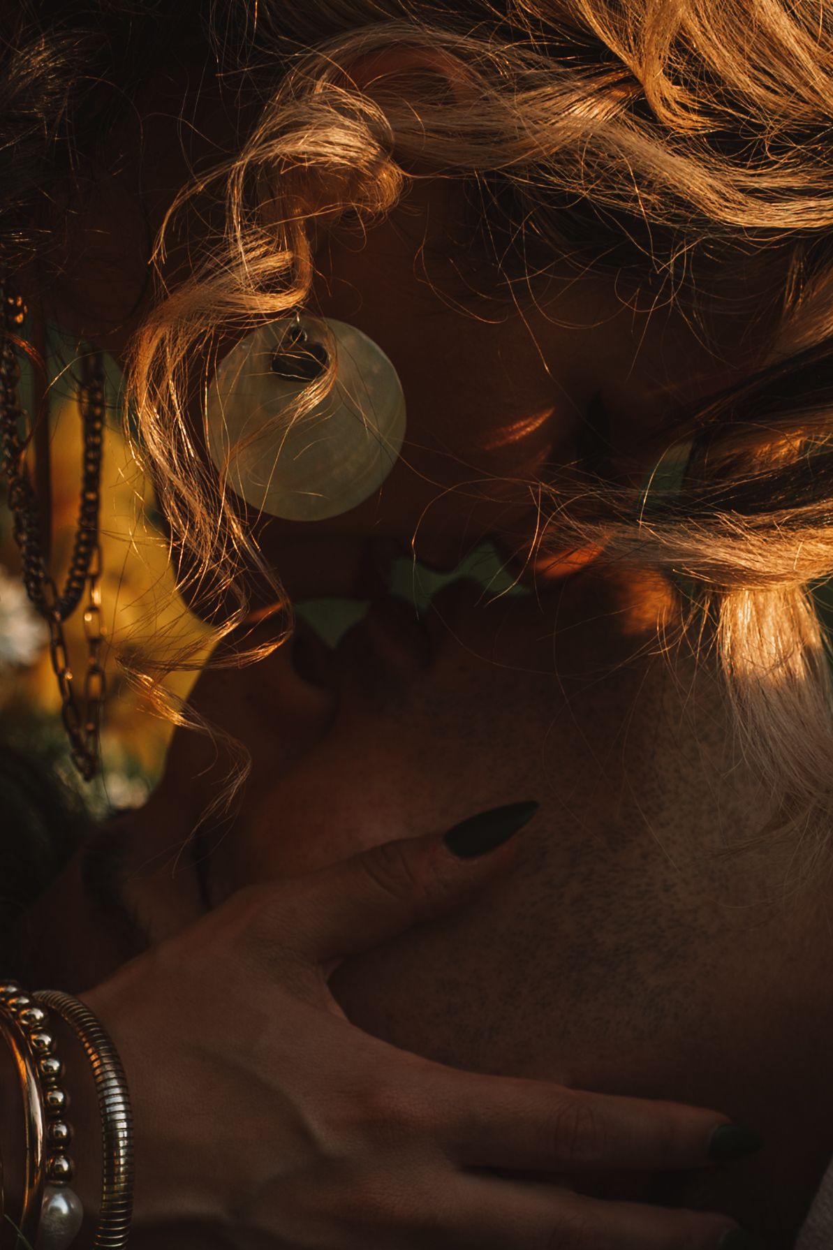 Close-up of woman with golden hair and hoop earring being embraced in warm sunset light. Taken by Row And Co Photography in FXBG VA