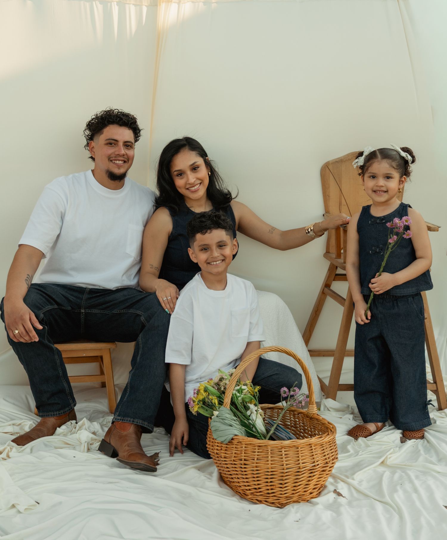 A happy family of four poses together with a wicker basket of flowers in a bright studio setting. Taken by Row And Co Photography in FXBG VA