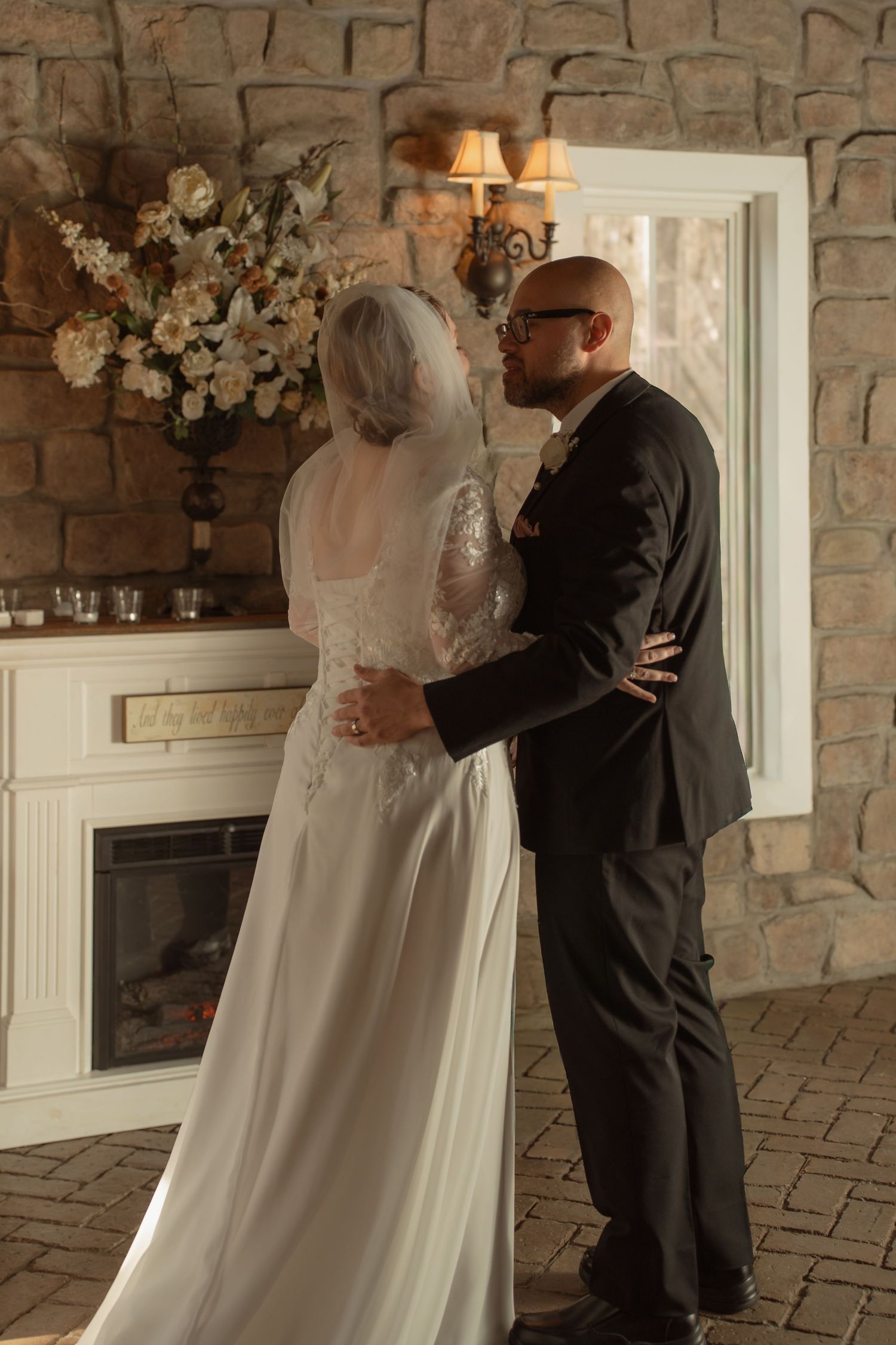 Bride and groom share a romantic kiss in front of a stone fireplace during their indoor wedding ceremony.