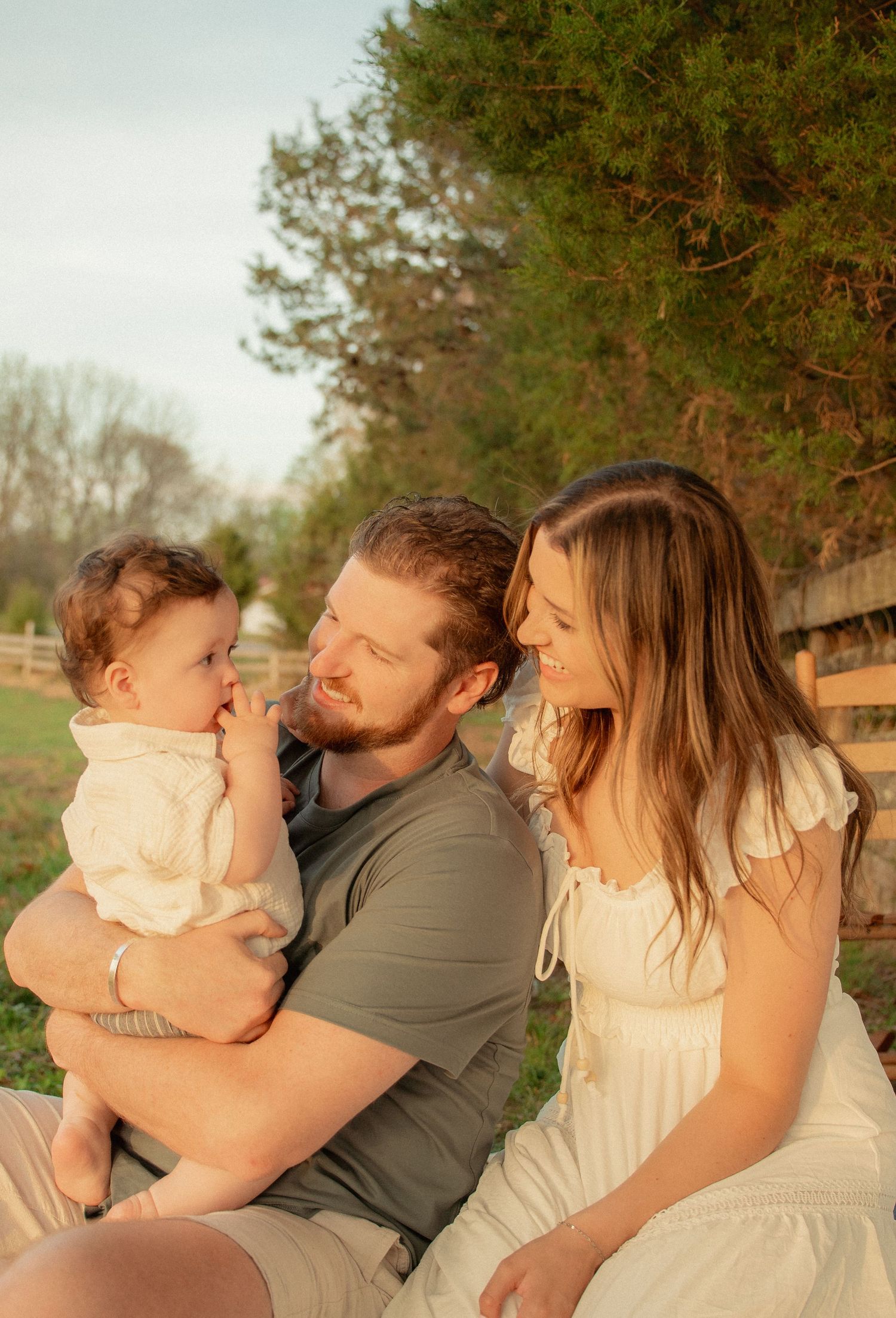 Young family with baby enjoying a warm golden hour moment outdoors near a wooden fence. Taken by Row And Co Photography in FXBG VA