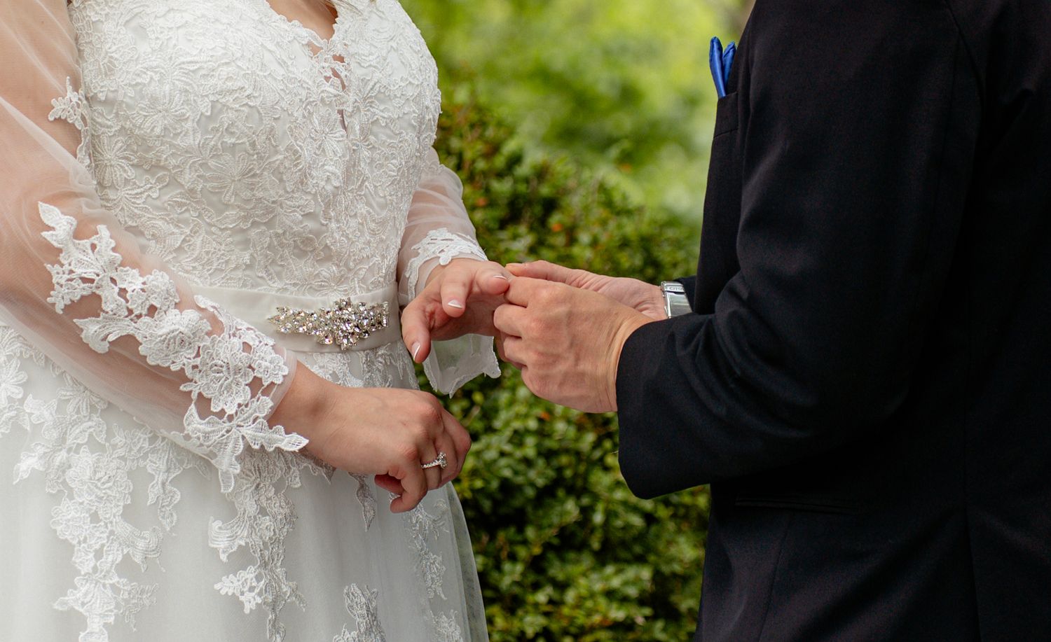 Groom placing a wedding ring on brides finger during outdoor ceremony, bride wearing lace long sleeve wedding gown. Row and Co Photography