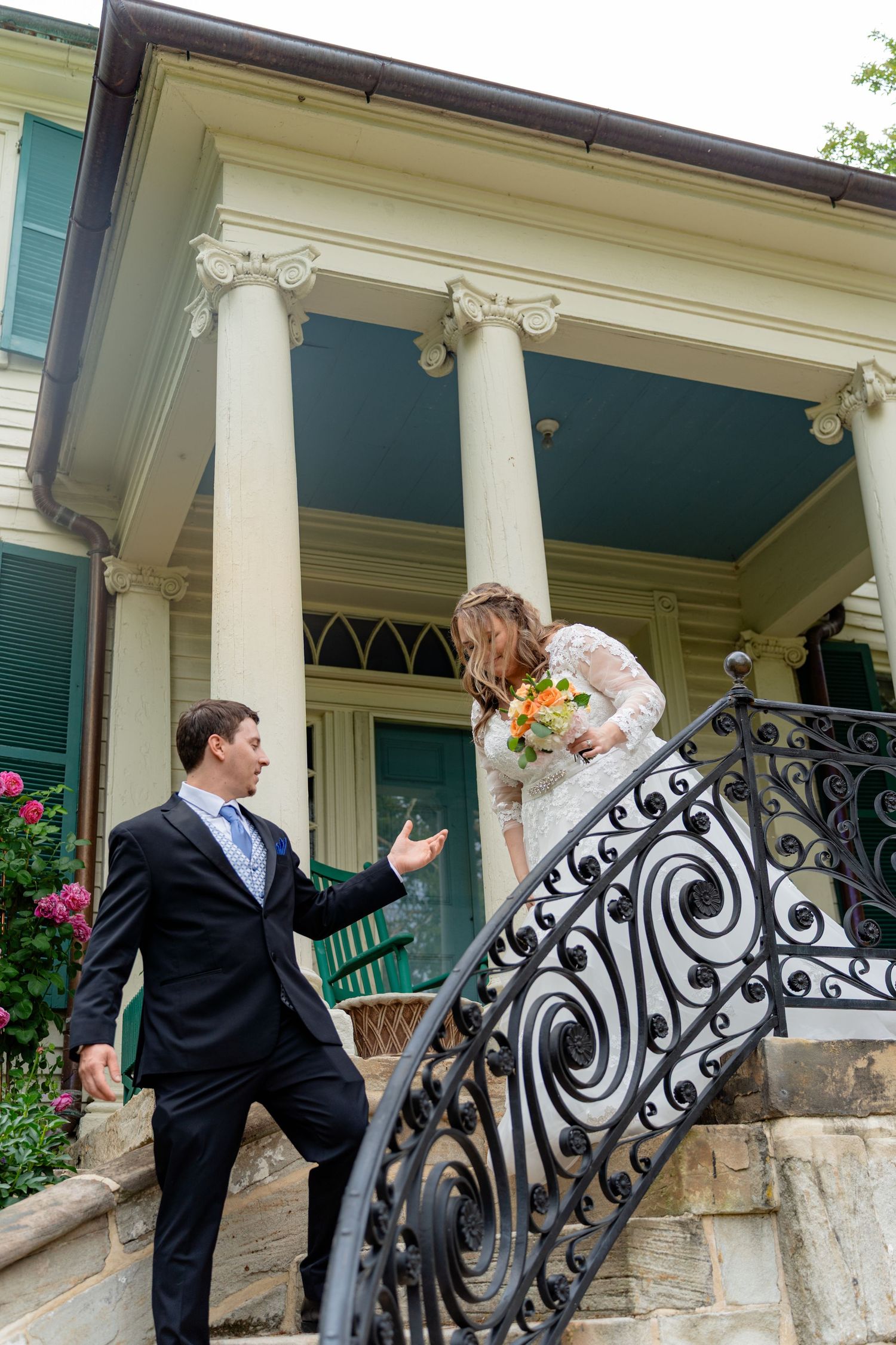 Bride and groom on ornate iron staircase outside elegant historic home with white columns.
