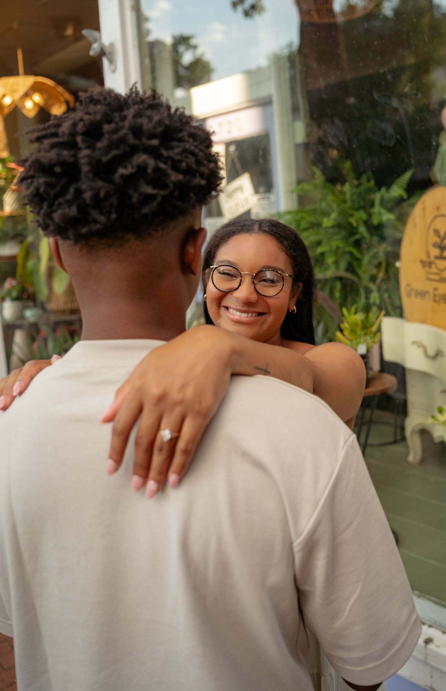 Smiling woman with glasses embracing her partner during an engagement photo session outside a shop. Taken by Row And Co Photography in FXBG