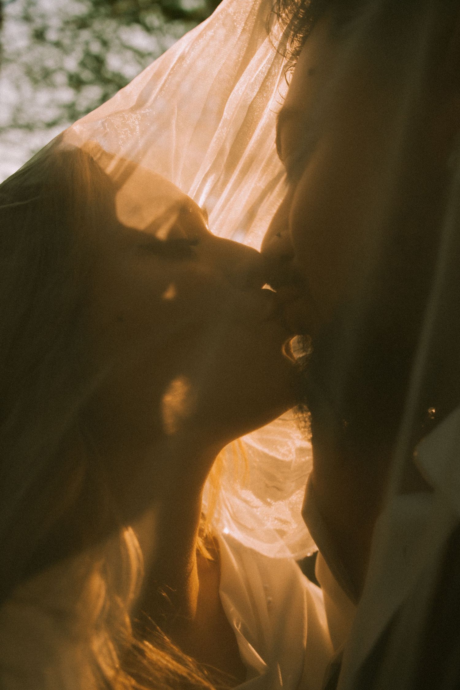 Romantic silhouette of a couple kissing through a sheer golden veil in warm sunset light.