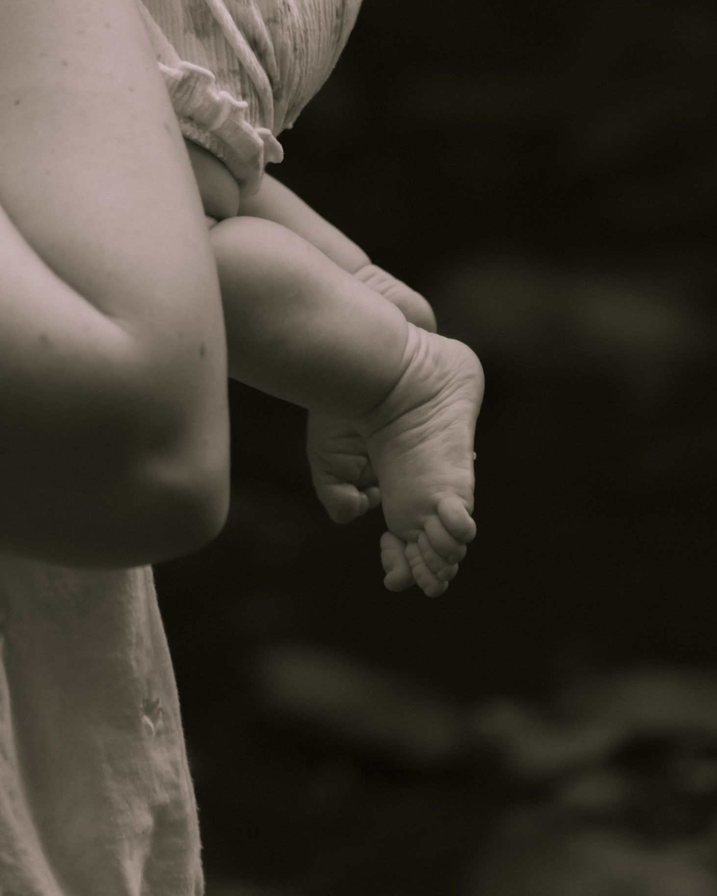 Close-up black and white photo of a mother holding her newborn baby, showcasing tiny infant feet and legs.