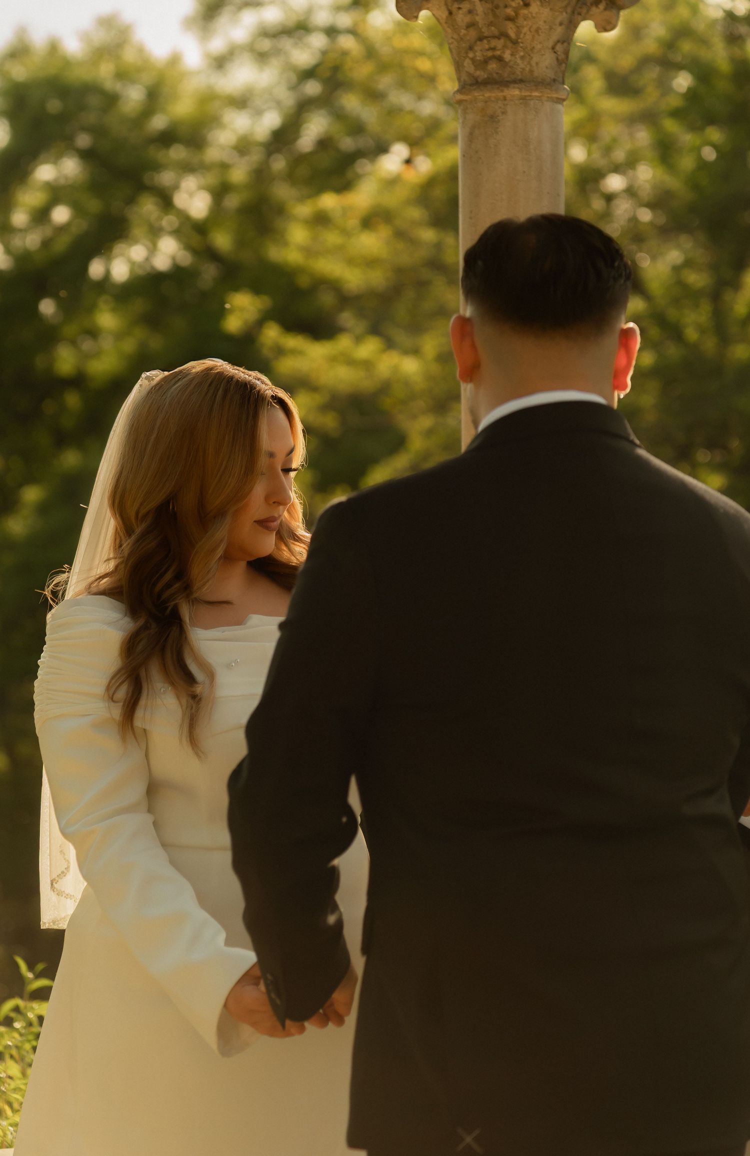 A bride in a white gown holds hands with a groom in a black suit during an outdoor wedding ceremony.