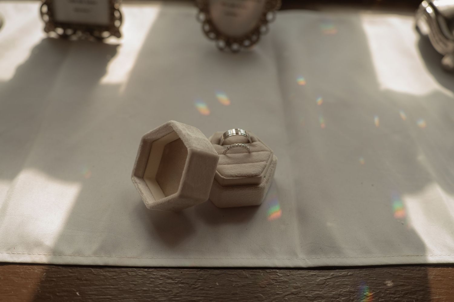 Diamond engagement ring displayed in an open hexagonal velvet ring box on a white linen surface with soft sunlight.