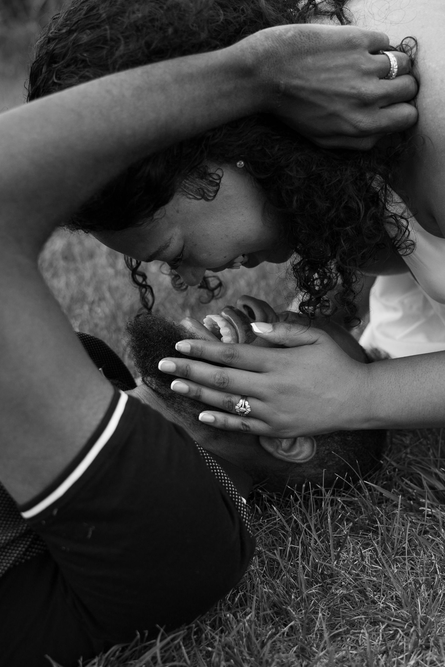 Black and white photo of a couple sharing an intimate moment, foreheads touching, with rings visible on their hands.