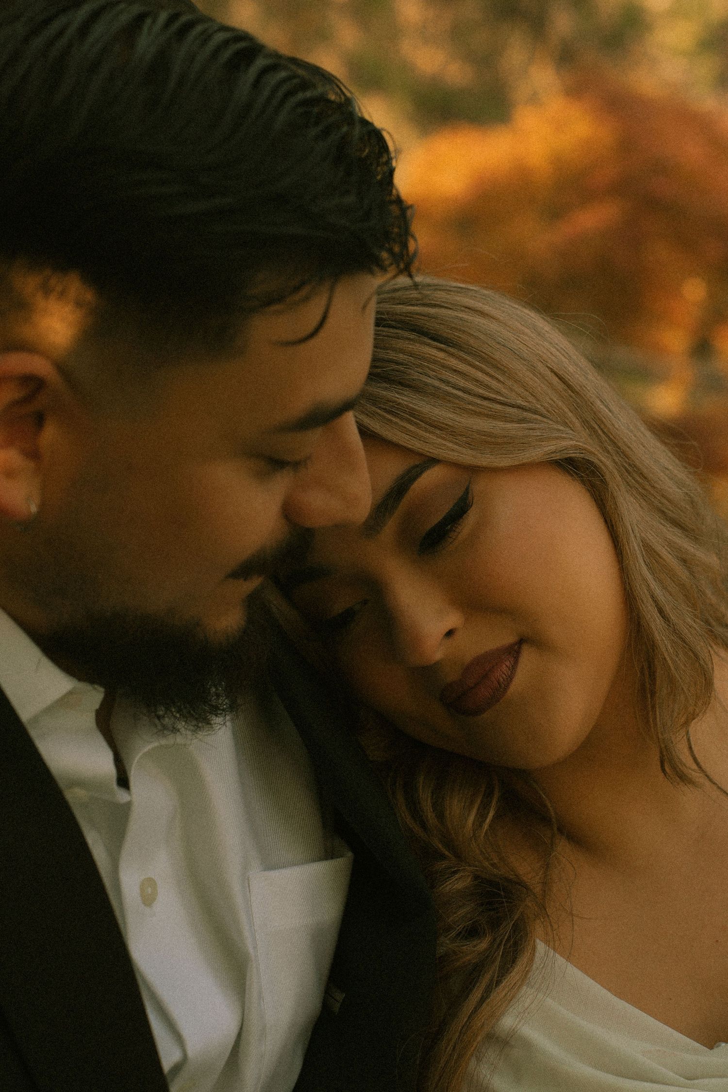 A couple in wedding attire sharing an intimate moment outdoors surrounded by warm autumn foliage.