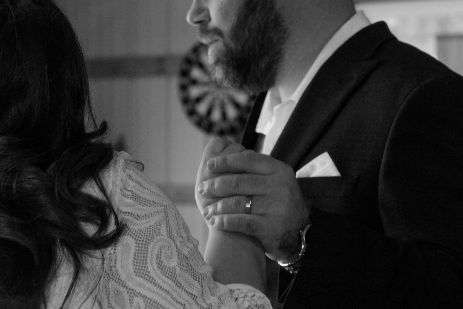 Black and white wedding photo of bride and groom holding hands, showcasing diamond ring and elegant lace dress.