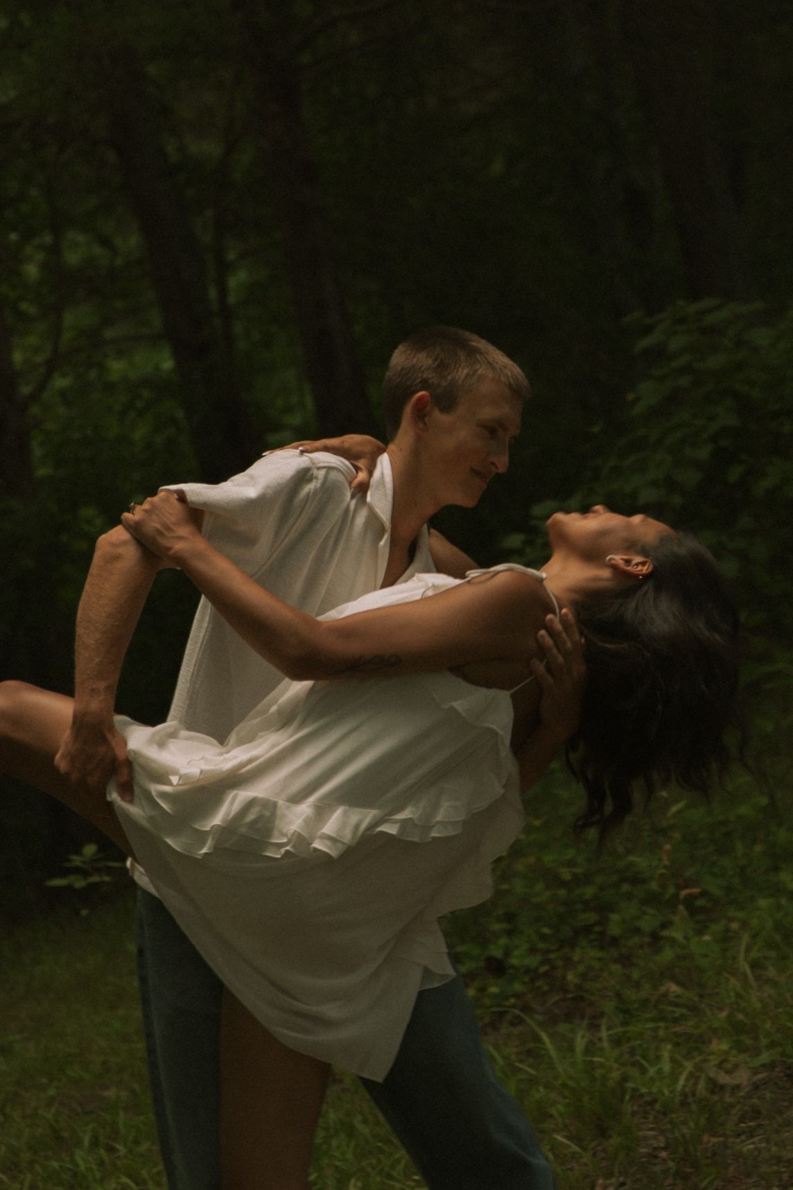 Couple dancing romantically in a lush green forest, man dipping woman in a graceful dance move outdoors.