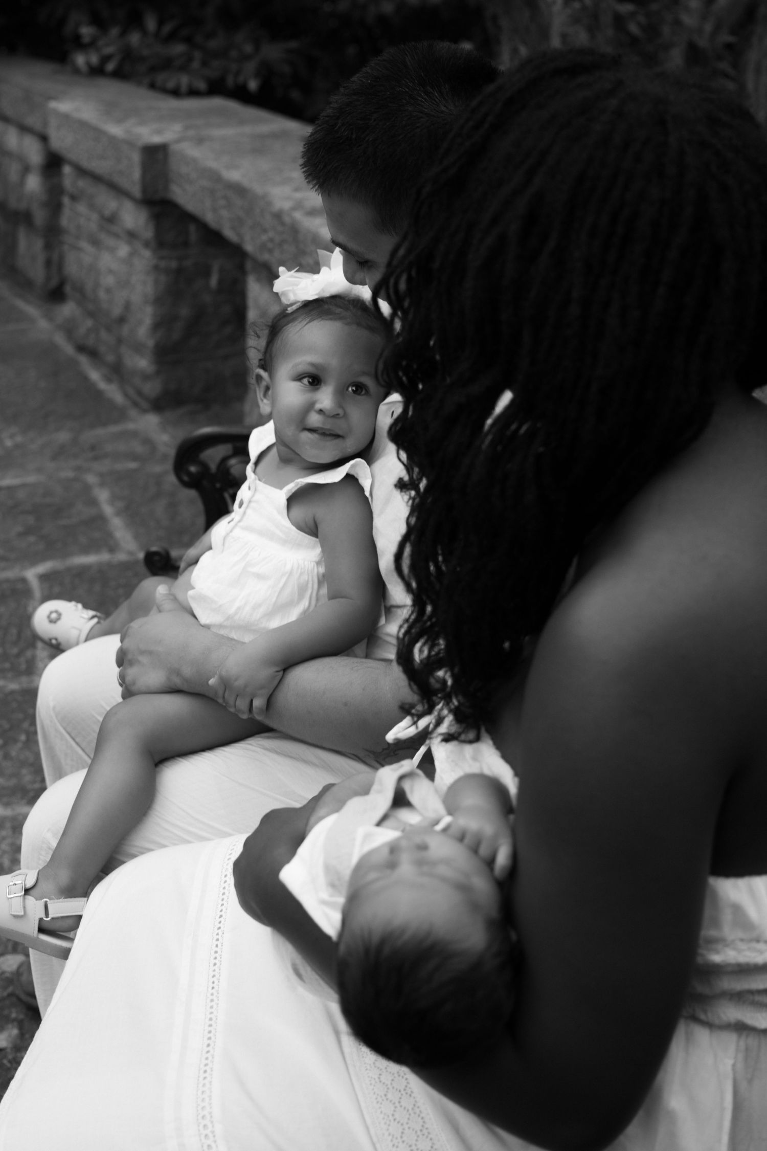 Black and white photo of a mother holding two babies outdoors, with the older infant smiling and wearing a white bow.