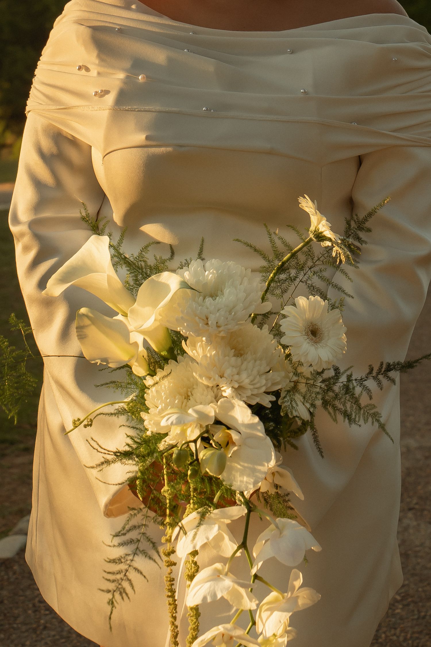 Bride in ivory satin gown holding elegant white wedding bouquet with calla lilies, gerbera daisies, and ferns.
